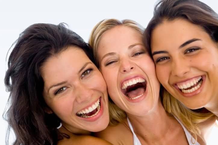 Three women laughing and smiling together, showcasing the joy and connection through laughter.