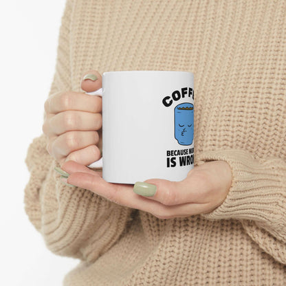 Person holding a ceramic coffee mug with a humorous design, featuring the text 'Coffee Because' in bold, against a cozy sweater background.