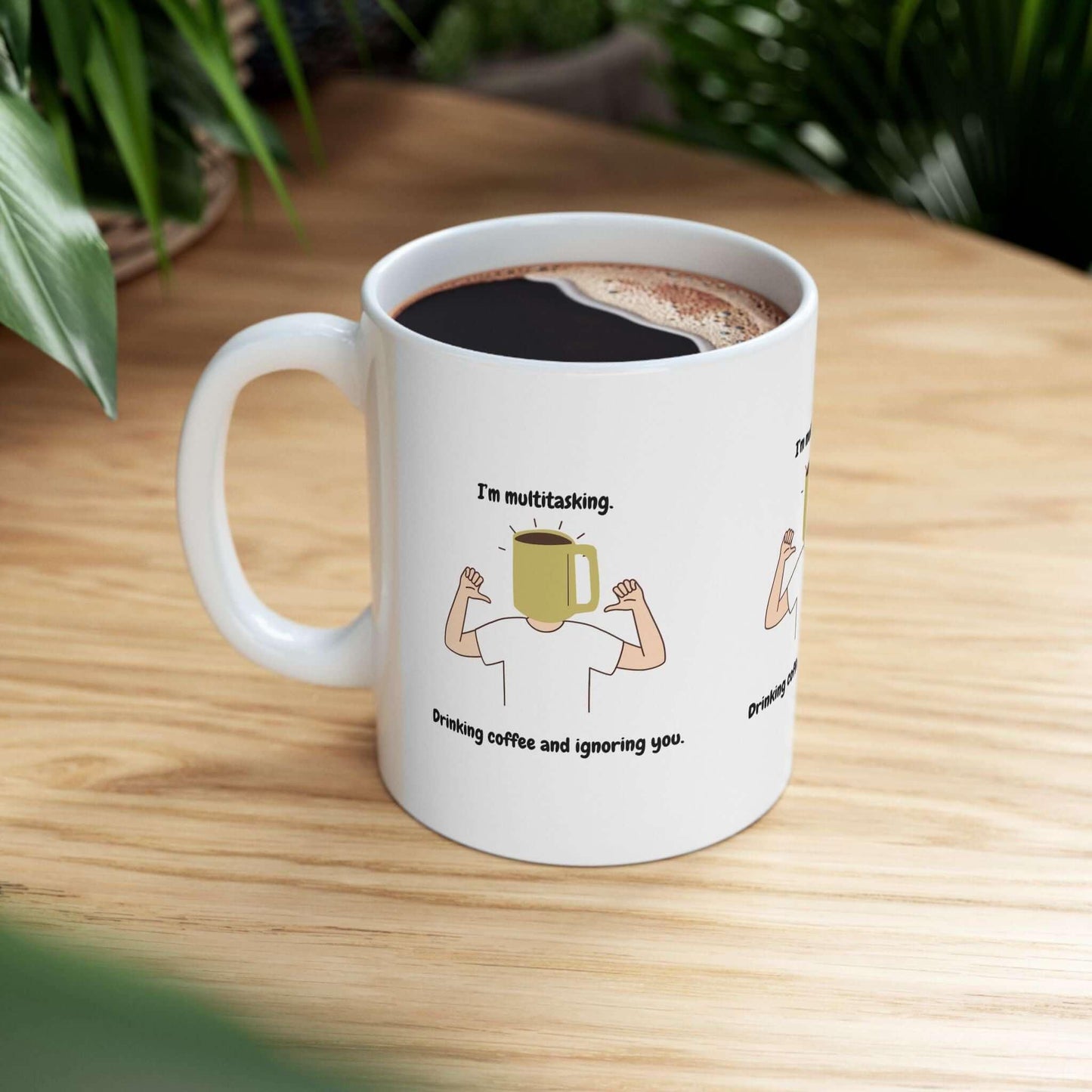 Funny ceramic coffee mug with a multitasking design, featuring a yellow mug character on a wooden table, surrounded by greenery.