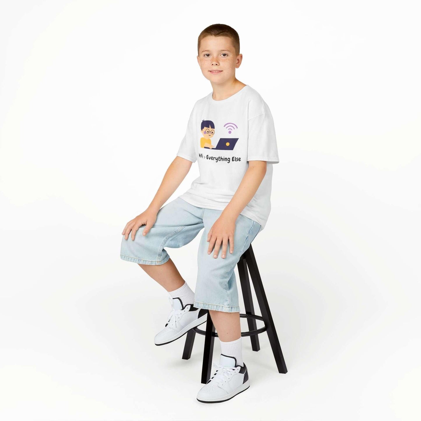 Young boy wearing a "Wifi Greater Than Everything" funny T-shirt, sitting on a stool, showcasing a comfortable kids' cotton tee.