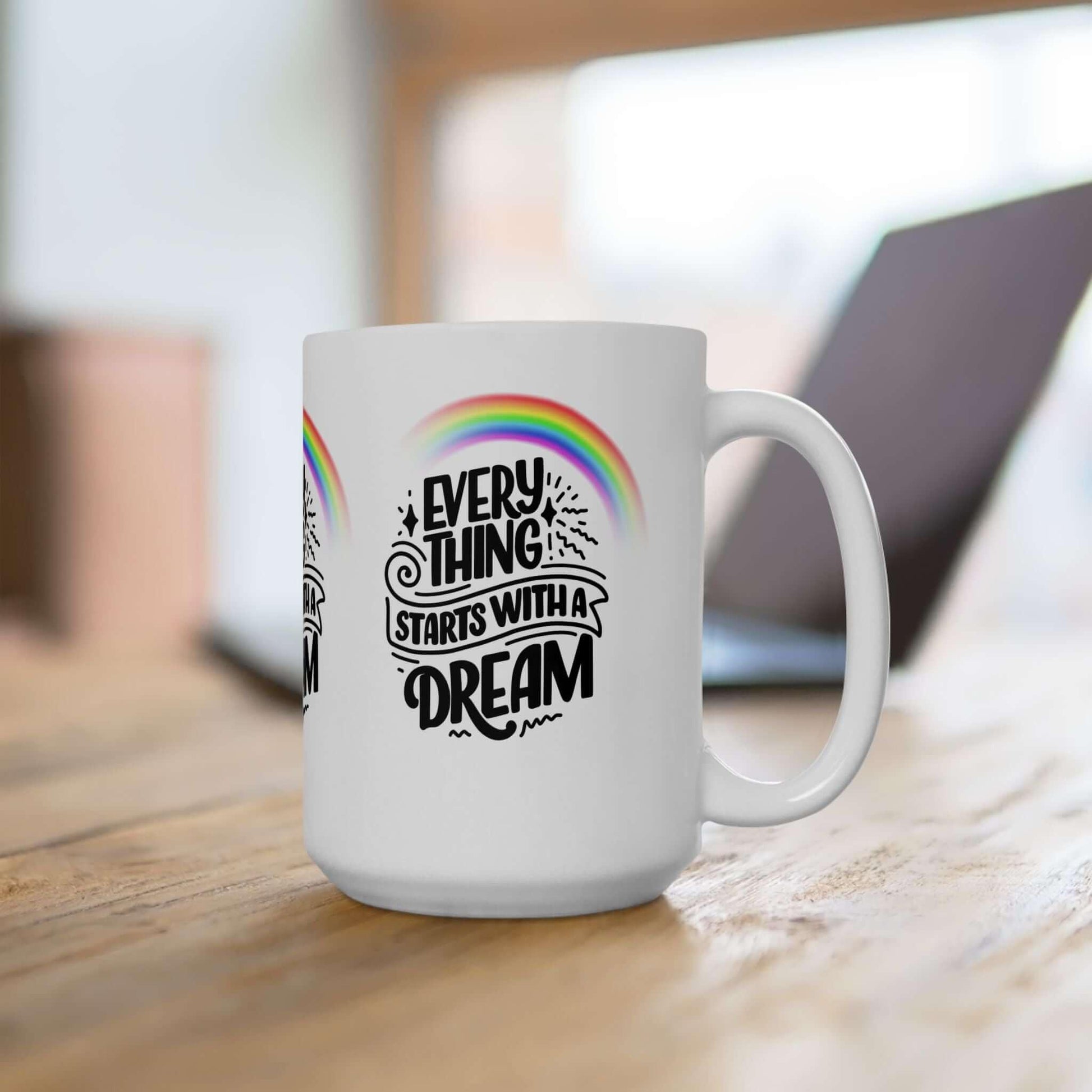 Ceramic coffee mug with 'Everything Starts with a Dream' text and rainbow design, placed on a wooden table, perfect for gifting.