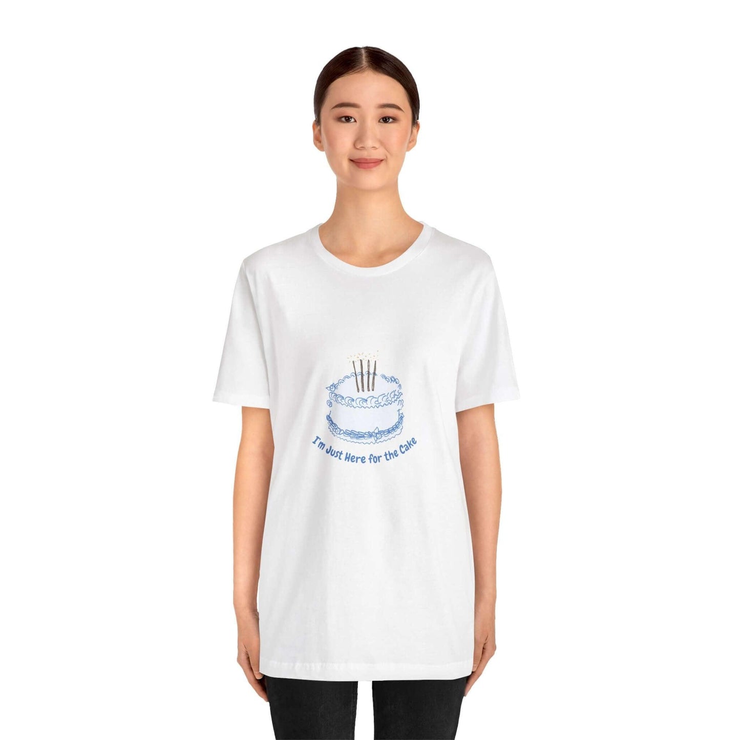 Woman wearing a funny t-shirt with 'I'm Just Here for the Cake' print, made of soft cotton with ribbed knit collar and tapered shoulders.