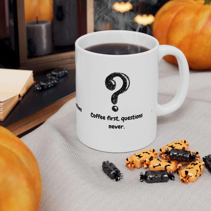 White ceramic mug with 'Coffee First, Questions Never' text, surrounded by black and orange candies, on a festive autumn-themed table.