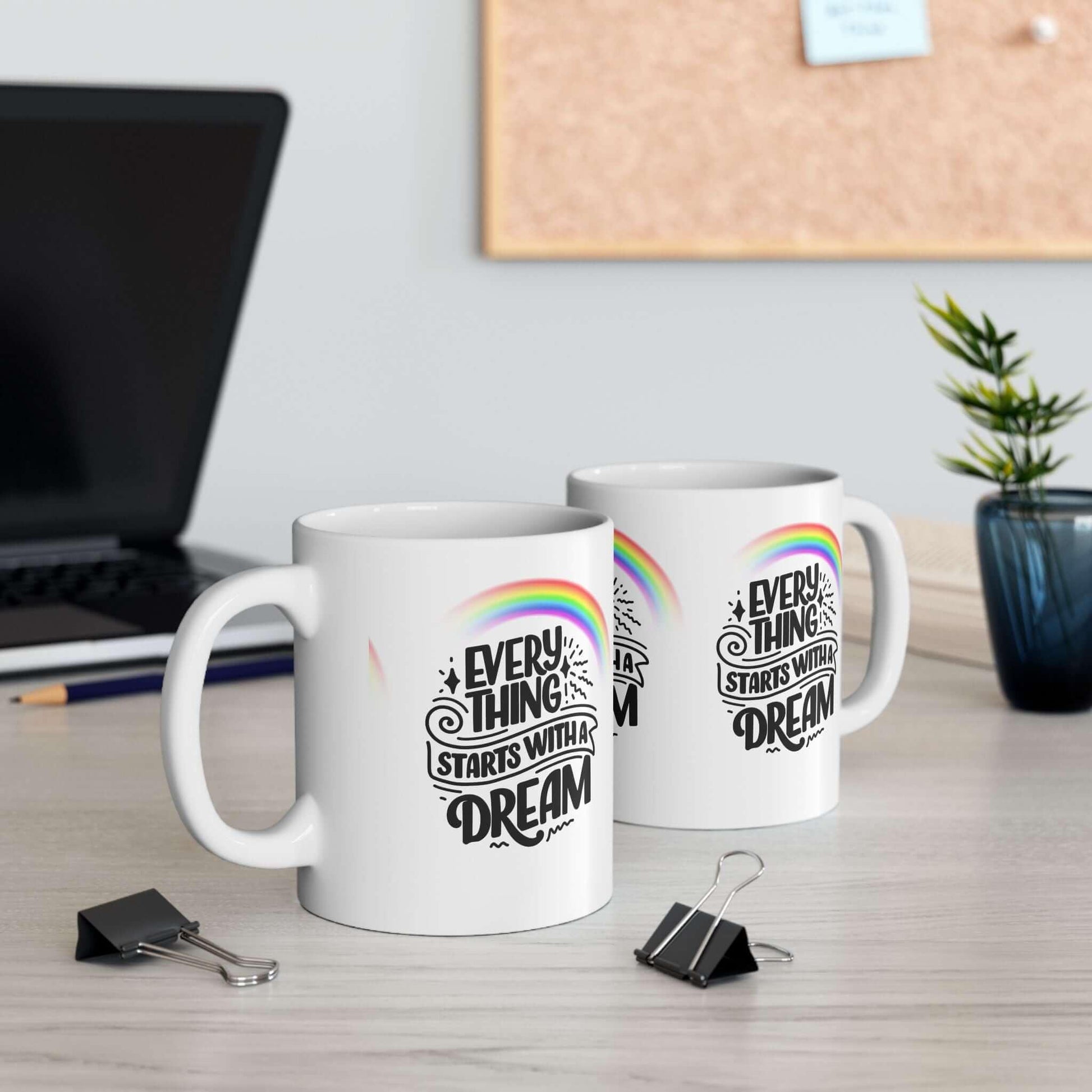 Two ceramic coffee mugs with 'Everything Starts with a Dream' design, rainbow graphic, on a desk, ideal for personalized gifting.