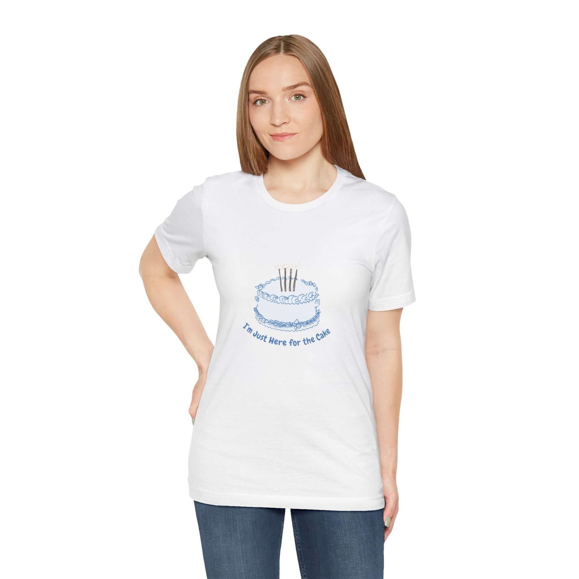 Woman wearing a white t-shirt with a funny cake graphic and "I'm Just Here for the Cake" text, jeans, neutral background.