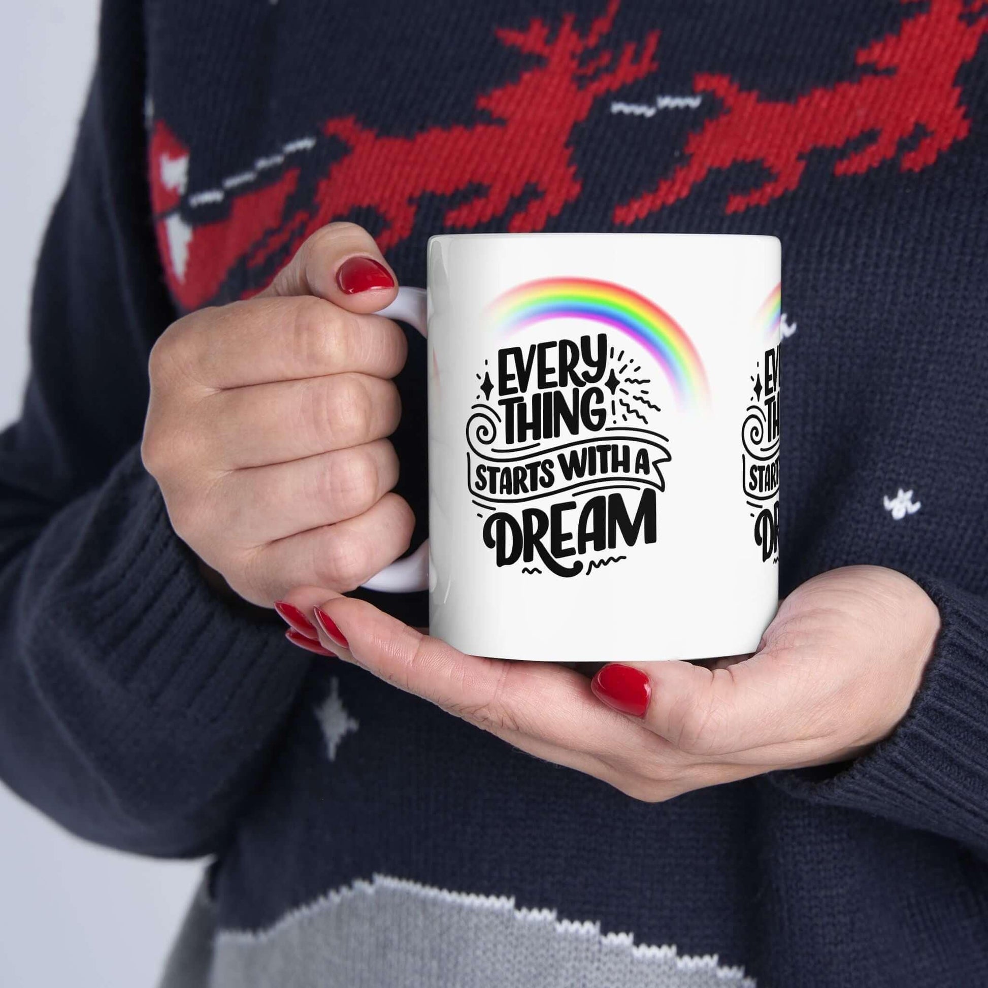 Person holding a ceramic coffee mug with 'Everything Starts with a Dream' design and rainbow, perfect gift idea.